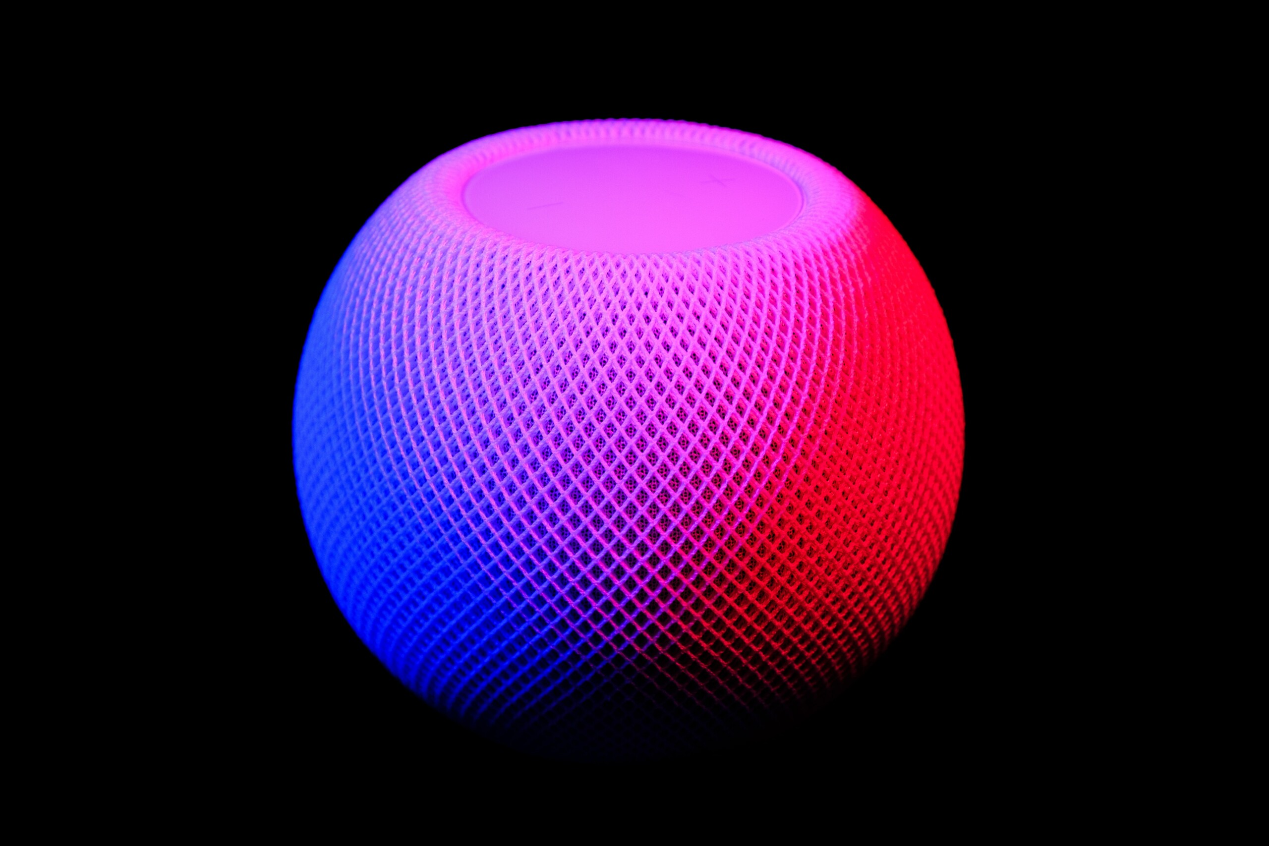 Le HomePod Mini sur un fond noir avec des reflets de couleur bleue, rose et rouge