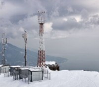 Relay station with towers on top of the rock in winter with mountain and sea on the background with overcast cloudy sky