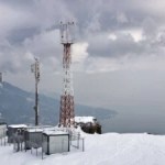 Relay station with towers on top of the rock in winter with mountain and sea on the background with overcast cloudy sky