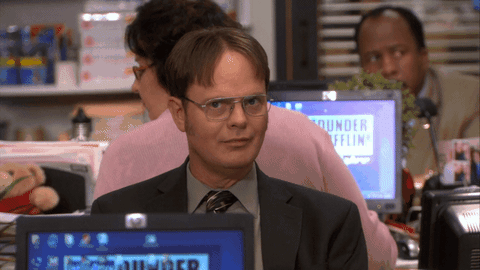 Dwight dans la série The Office mimant le signe du secret avec son doigt.