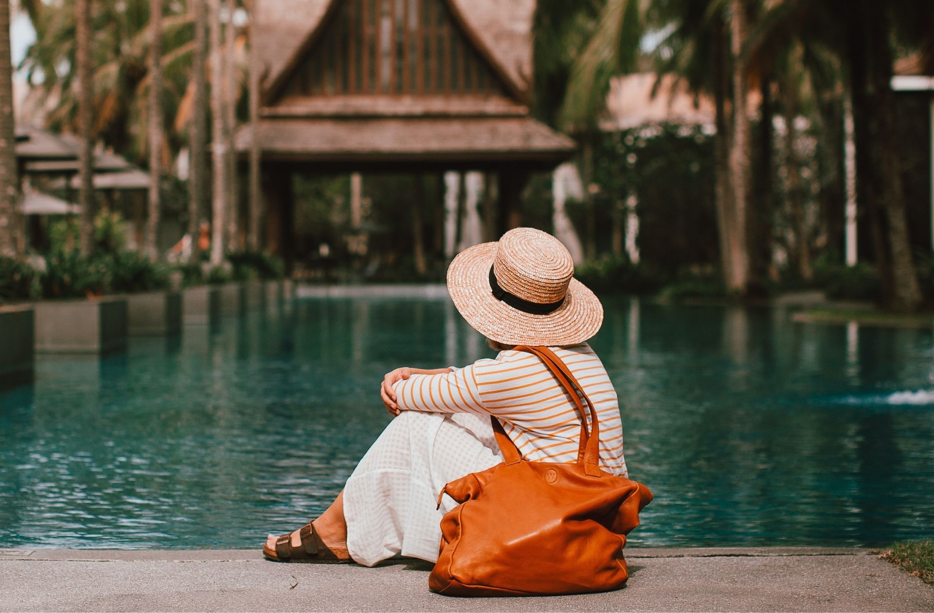 Femme avec un sac 48h à l'épaule, assise devant une piscine