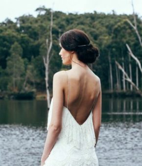 Une femme en robe de mariée dos-nu se tient devant une étendue d'eau