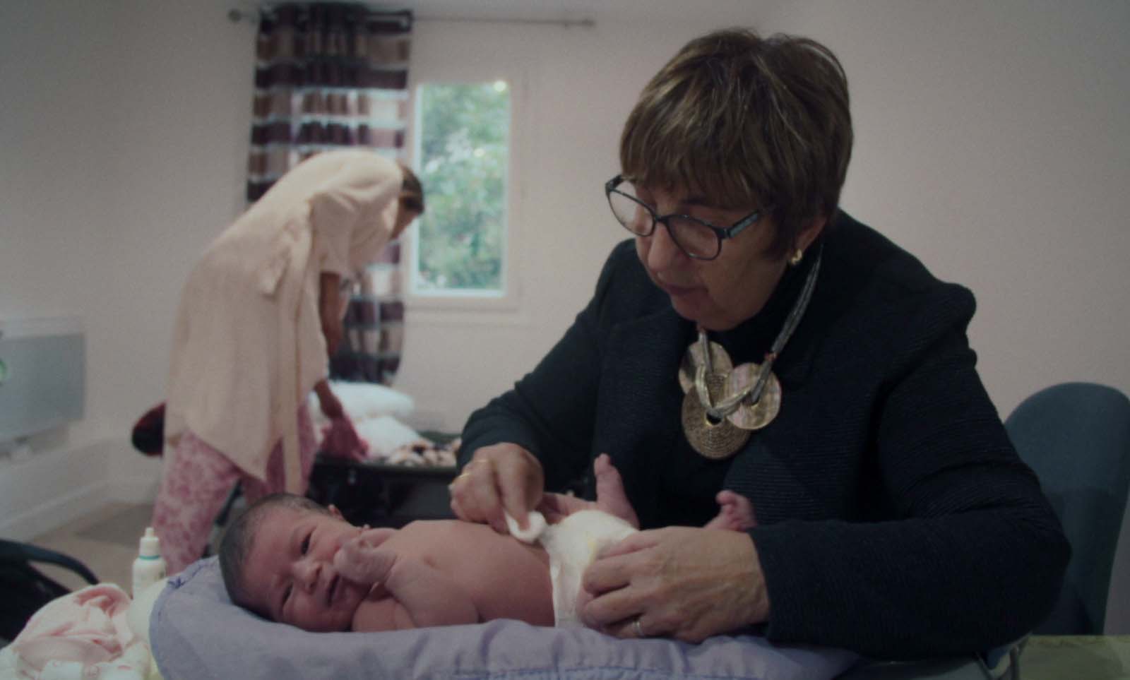 Chantal Birman, une sage-femme âgée, s'occupe d'un bébé dont elle change la couche.