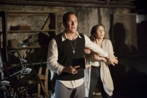 Le héros du film Conjuring, un exorciste, place derrière lui son épouse et associée. Ils ont l'air effrayés. Le héros du film Conjuring, un exorciste, place derrière lui son épouse et associée. Ils ont l'air effrayés.