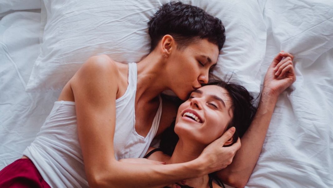Deux femmes amoureusement enlacées sur un lit.