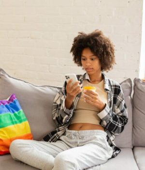 Personne assise sur un canapé avec un coussin LBGT, téléphone à la main