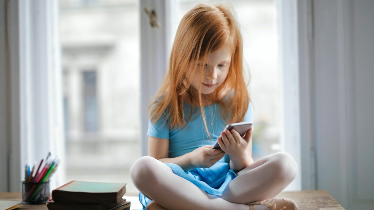 Enfant assise sur une table, un smartphone à la main Enfant assise sur une table, un smartphone à la main