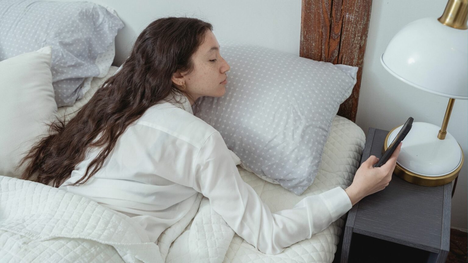 Femme dans son lit lisant un SMS sur son smartphone