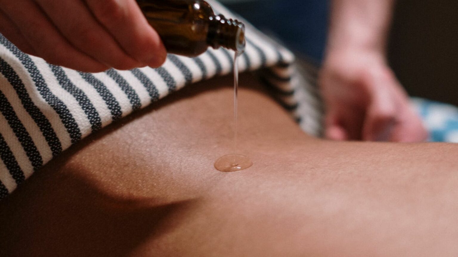Une personne verse de l'huile de massage sur le dos d'une autre personne. Une personne verse de l'huile de massage sur le dos d'une autre personne.