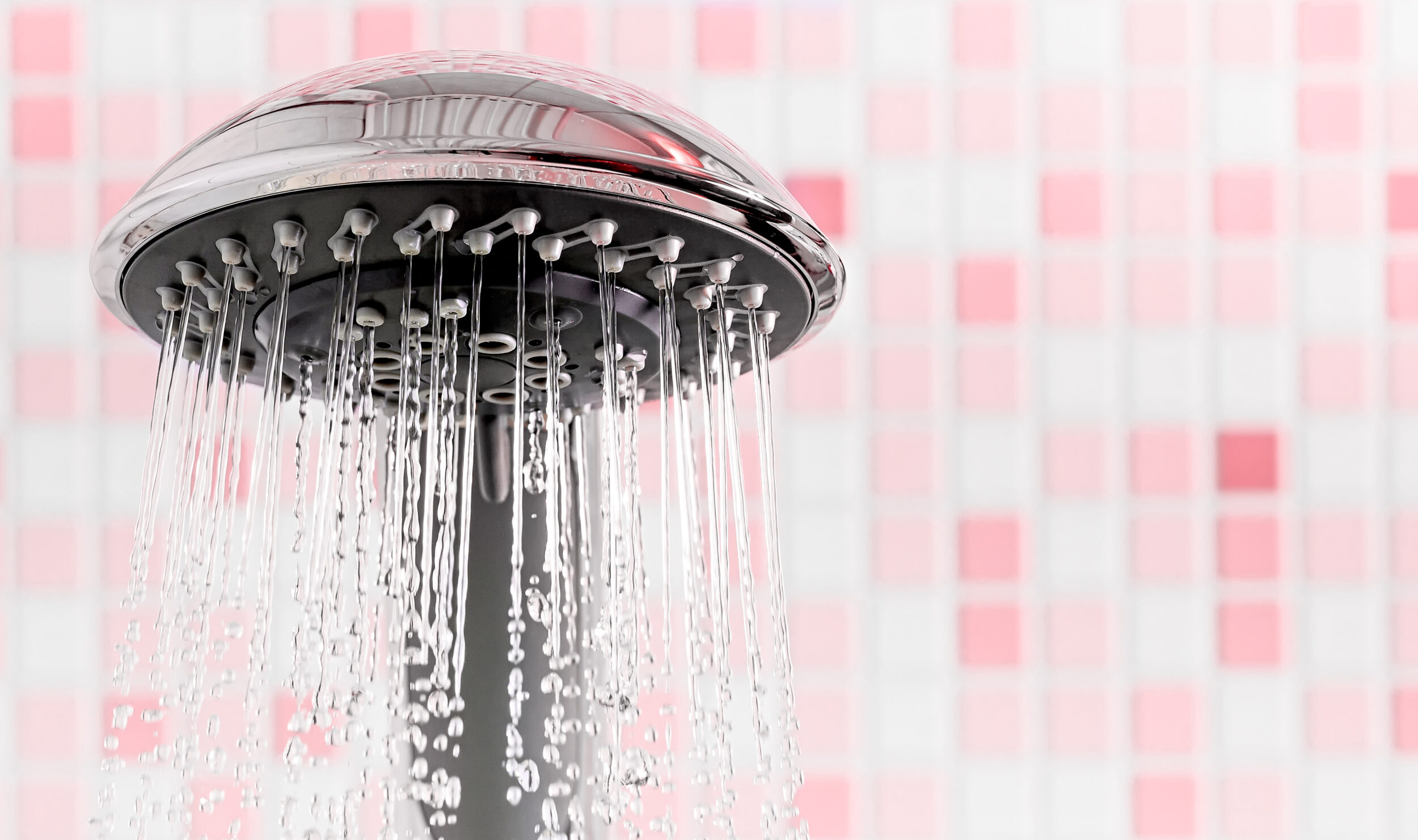 Modern Shower head with running water in pink bathroom. Copy space