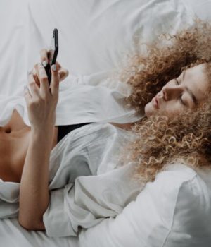 Une femme dénudée allongée dans son lit, en train de consulter son téléphone portable