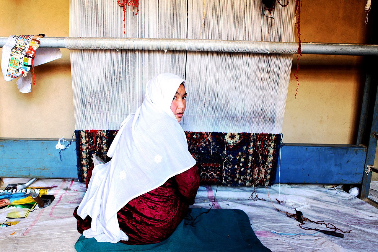 An Afghan woman breaks away from weaving an Afghan rug in her home in the Dragon Valley region of Bamyan, Afghanistan, an area that was once a Taliban stronghold. The woman is employed by Arzu Studio Hope, a nonprofit organization that provides income to Afghan women by sourcing and selling the rugs they weave. Arzu helps weavers and their families break the cycle of poverty by providing them above market compensation and access to education and healthcare. Arzu founder, Connie Duckworth, visited Helmand province in search of possible locations to expand the organization.