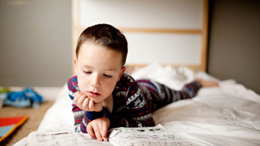 Un enfant allongé en train de lire un livre // Source : Gemutlichkeit
