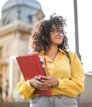 Une étudiante tenant des classeurs devant une université // Source : pexels-andrea-piacquadio