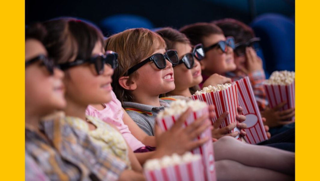 Des enfants en train de regarder un film au cinéma avec du popcorn © Andresr de la part de Getty Images Signature via Canva