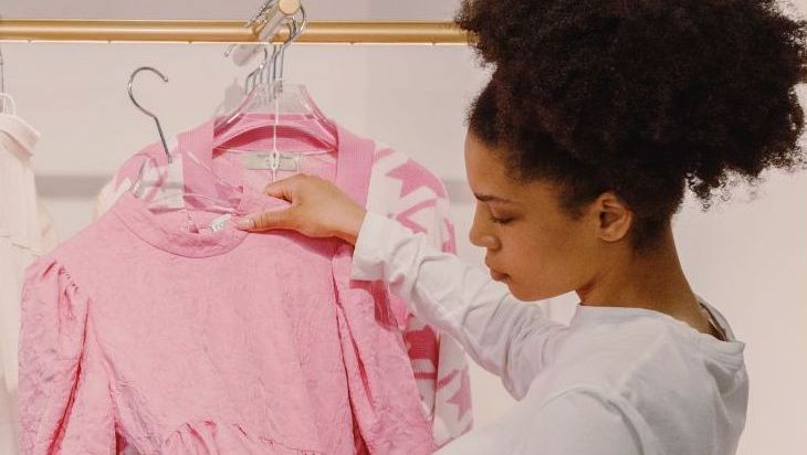 Une femme en train de considérer un vêtement dans un rayon de boutique © Ron Lach de la part de Pexels via Canva