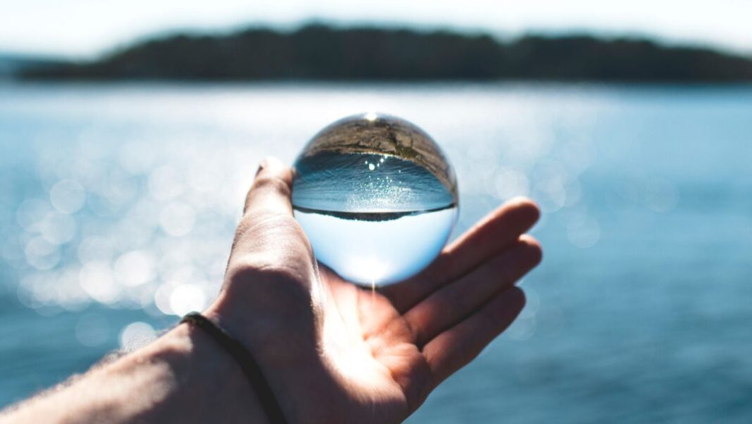 Une main tenant une bille de verre devant un plan d'eau // Source : Sindre Strom de Pexels