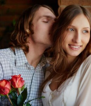 Un homme en train d'embrasser les cheveux d'une femme et de lui offrir des roses // Source : Shironosov de la part de Getty Images
