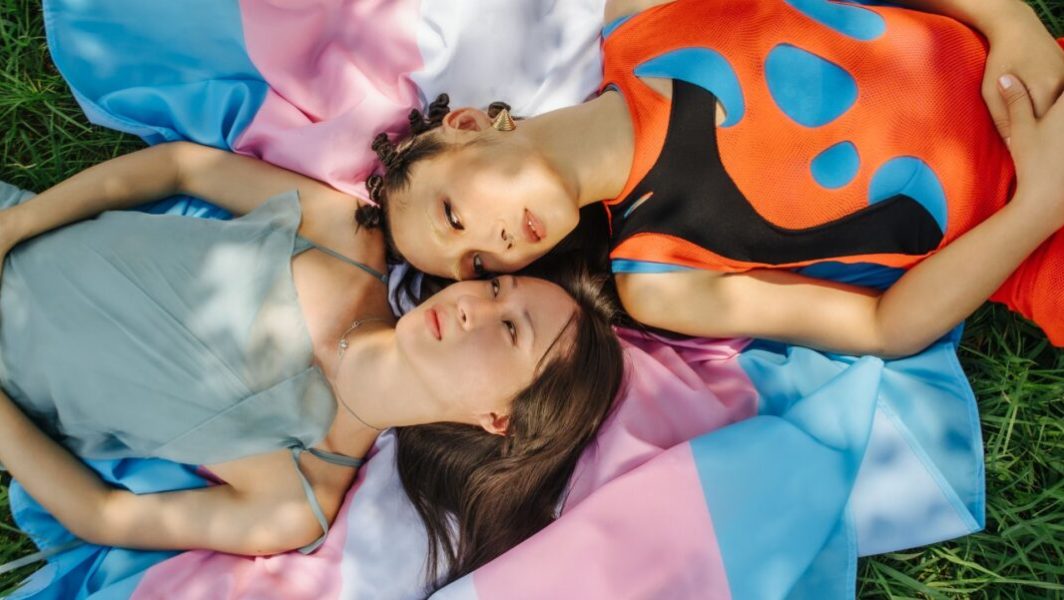Deux personnes se regardant avec tendresse allongées sur le drapeau trans rose, blanc et bleu // Source : Lindsay Ryklief de Lindsay Ryklief