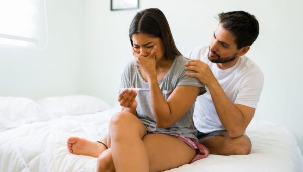 Un homme et une femme en larmes face à un test de grossesse // Source : Antonio Diaz de Getty images