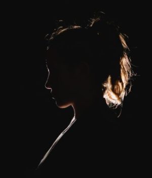 Une silhouette de fillette avec une queue de cheval, photographiée dans le noir // Source : Unsplash / Molly Blackbird 