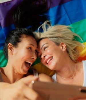 Deux femmes lesbiennes en train de faire un selfie devant un drapeau LGBT+ // Source : PixelsEffect de Getty Images Signature