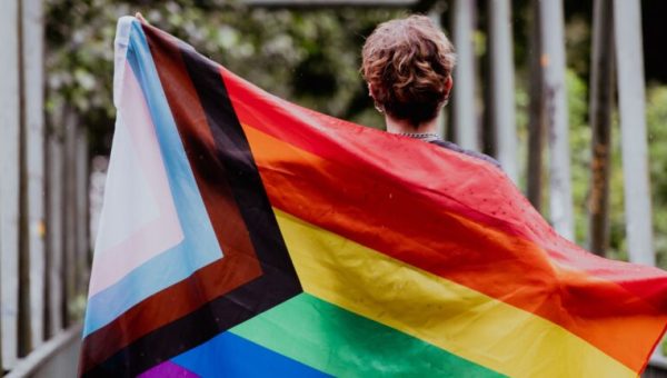 Une personne de dos, tenant le drapeau des fiertés LGBTI // Source : Emma Rahmani de baseimage