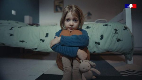 Une petite fille a l'air inquiète, assise au pied de son lit avec un doudou à la main, car elle est victime de violence sexuelle de la part d'un membre de sa famille // Source : Capture d'écran d'une campagne nationale du gouvernement sur l'inceste