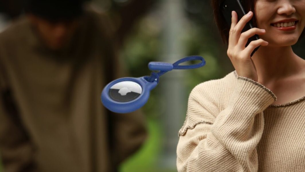 Une femme sourit au téléphone pendant qu'un homme rôde derrière elle, parce qu'il a pu la stalker grâce à un airtag qu'il a caché sur elle à son insu // Source : e yamasan de Getty Images