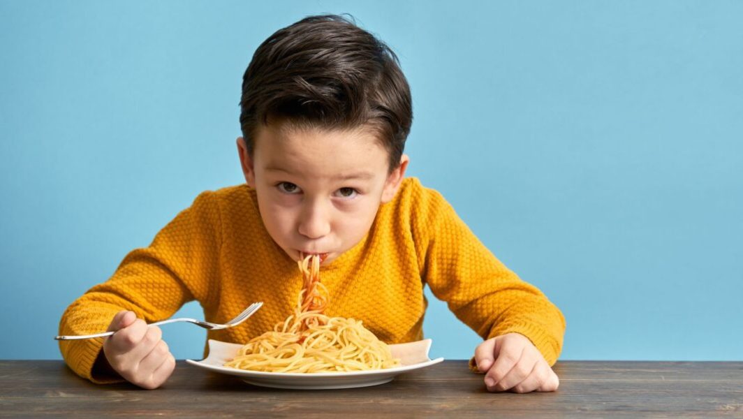 Un enfant en pull jaune en train de manger un plat de pâtes au ketchup // Source : pinstock de Getty Images Signature