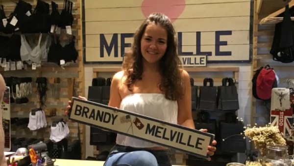 Une femme pose avec un panneau au logo de la marque Brandy Melville, au sein d'une boutique // Source : Capture d'écran YouTube de la bande-annonce du documentaire "Brandy Hellville & The Cult of Fast Fashion"