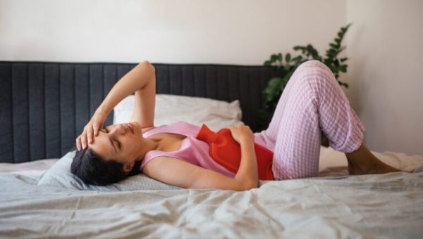 Woman at home suffering from menstrual pain. Menstrual cramps, woman warming the lower abdomen with a hot water bottle, endometriosis, and diseases causing pain.