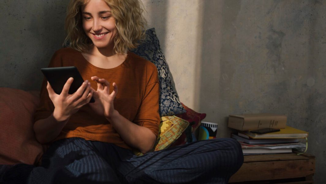 Portrait of smiling young woman sitting on bed using E-book reader