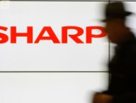 A pedestrian walks past a logo of Sharp Corp at a train station in Tokyo in this February 3, 2014 file photo. Embattled Japanese electronics maker Sharp Corp is preparing to seek aid from its two main lenders, a source with direct knowledge of the matter said, as it expects impairment losses from unprofitable businesses to mount this year.  REUTERS/Yuya Shino/Files (JAPAN - Tags: BUSINESS LOGO)
