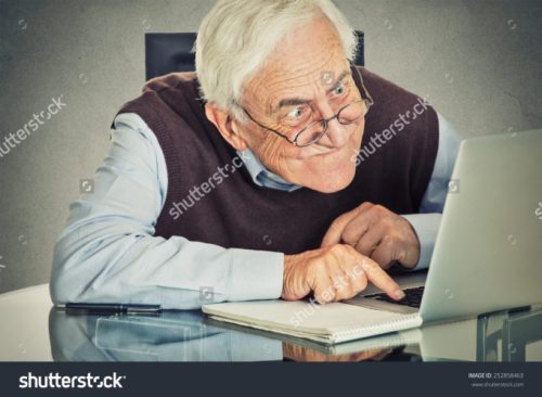 stock-photo-elderly-old-man-using-computer-sitting-at-table-isolated-on-grey-wall-background-senior-people-and-252858463