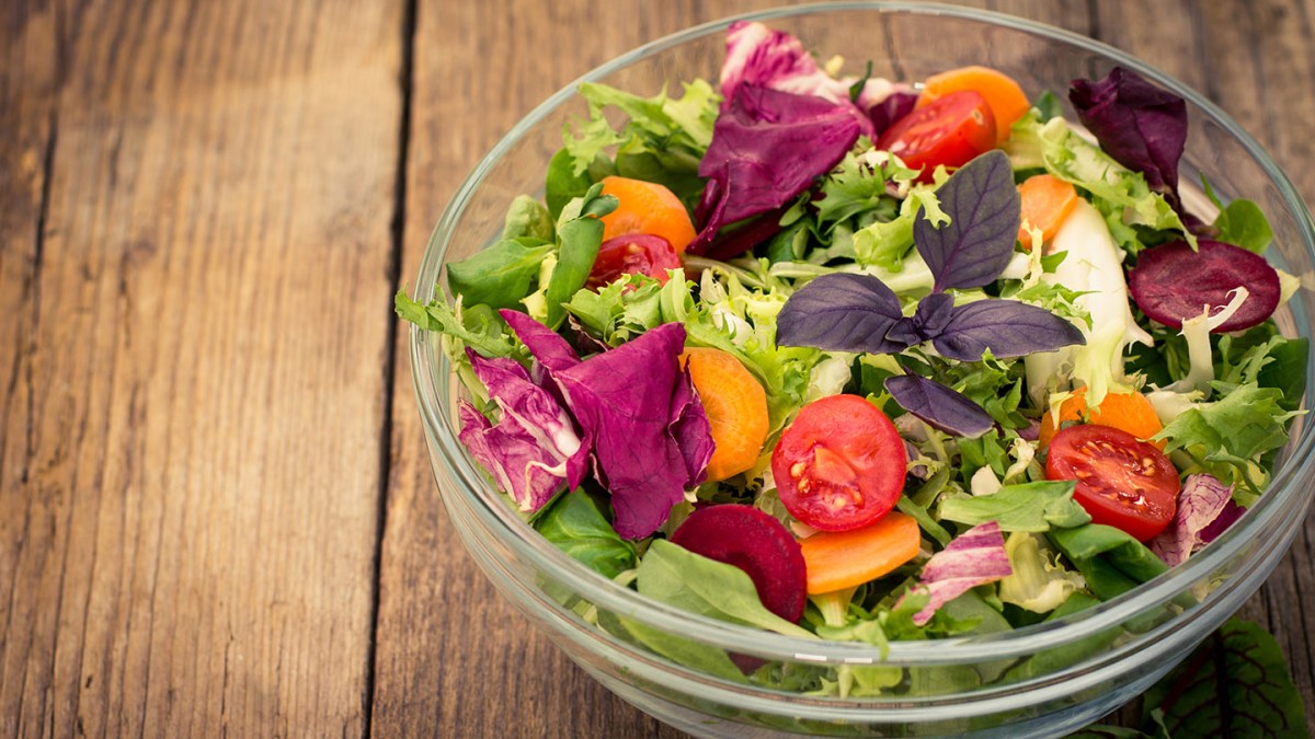 Fresh mixed salad in the bowl on the wooden table