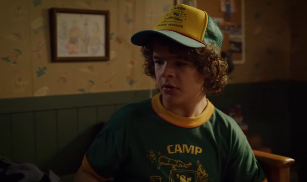 Dustin porte une casquette et un t Shirt « Camp Know Where » dans la saison 3. // Source : Youtube/Netflix