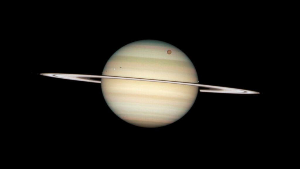 Transit of the moons Titan (largest at top right) and Enceladus, Dione and Mimas (from left to right, closer to the rings).  // Source: Flickr/CC/Nasa Hubble Space Telescope (cropped photo)