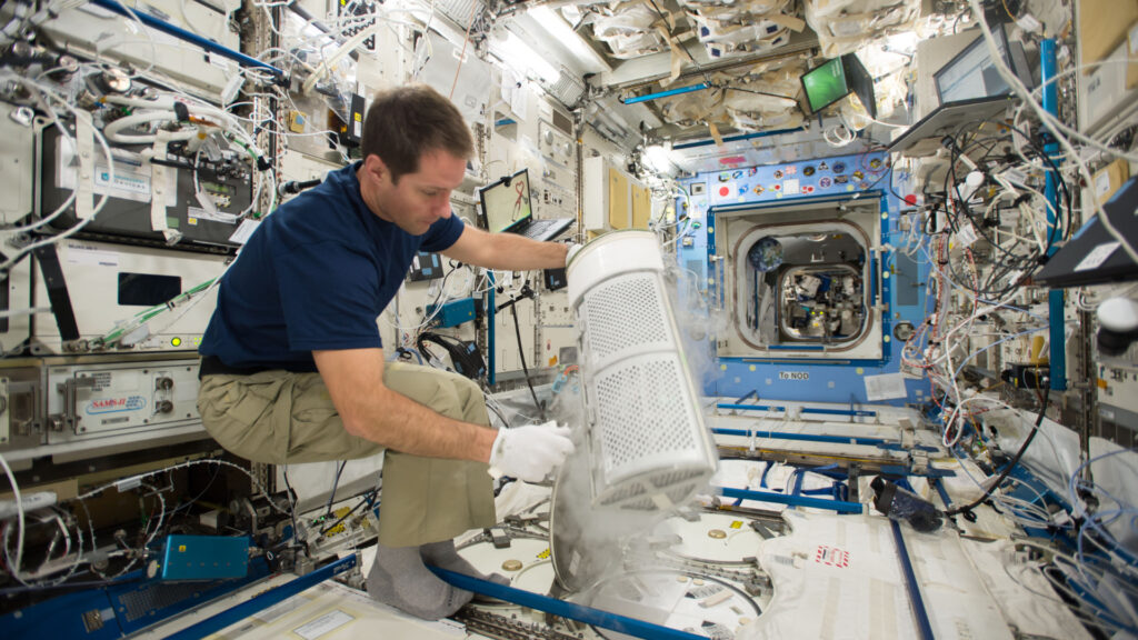 Thomas Pesquet insérant les tubes de prélèvements sanguins de l'expérience MARROW dans un congélateur, à bord de l'ISS, en 2016. // Source : Nasa (photo recadrée)