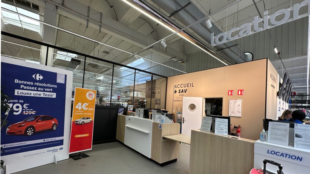 L'agence Carrefour Location est collée à l'accueil du magasin. Deux voitures sont mises en avant : la Dacia et la Tesla. // Source : Numerama