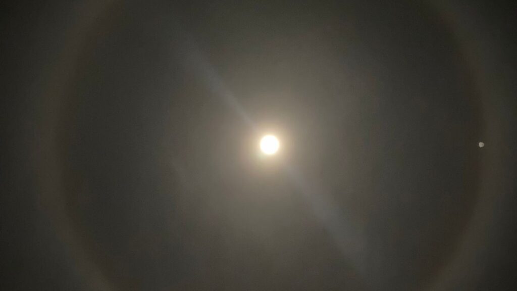 Spot on the camera?  No, lunar halo.  // Source: Via X @Pelut64 (cropped photo)