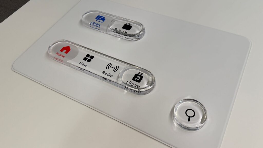 Les nouveaux boutons d'Apple Music ont été testés avec des maquettes, pour reproduire le vrai verre et ses reflets. // Source : Numerama