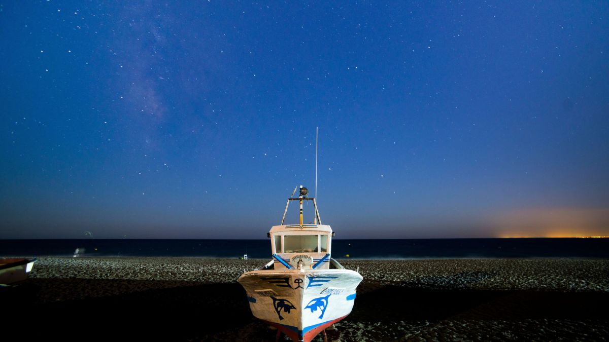 Bateau échoué sur une plage, sous un ciel étoilé. // Source : Canva