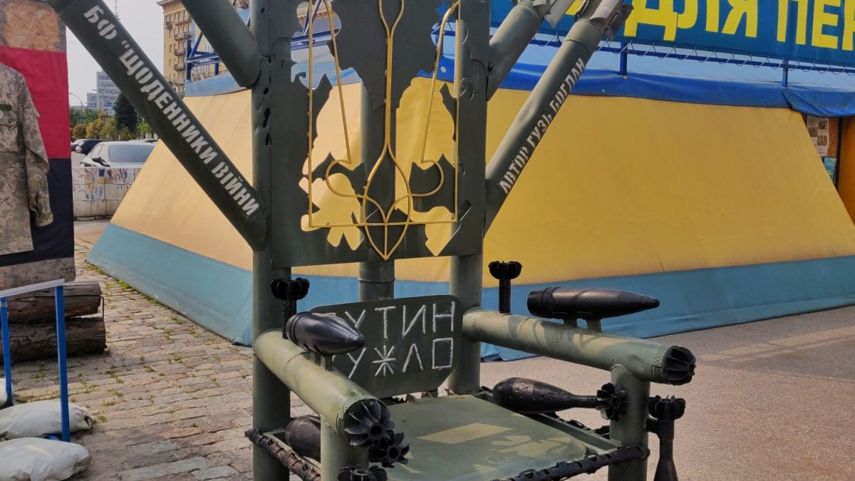 Trône de Fer en obus et roquettes devant des drapeaux ukrainiens.